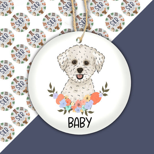 A ceramic Christmas decoration featuring an illustration of a Bichon Frise dog with a floral wreath and the text 'BABY'.