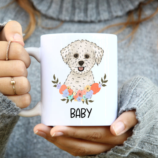 A person holding a white coffee mug with a colourful floral design and an illustration of a Bichon Frise dog breed.