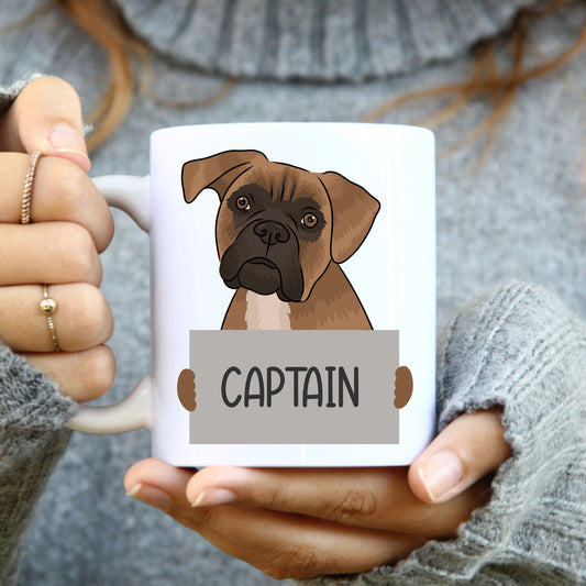 A person holding a white coffee mug with a colourful illustration of a boxer dog on it.