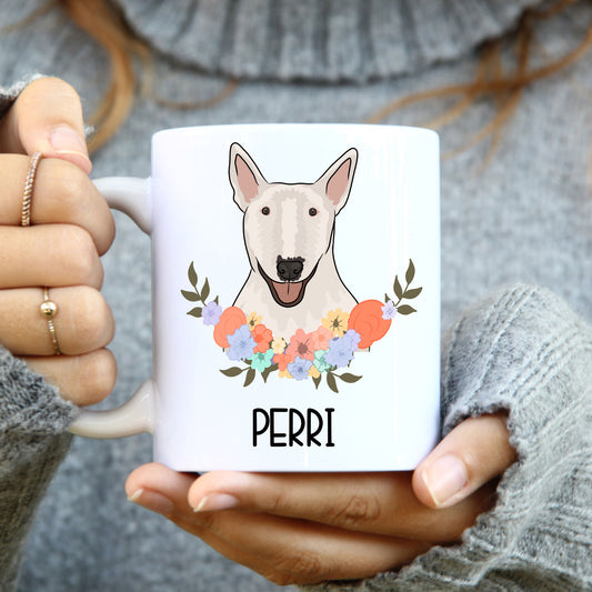 A person holding a white coffee mug with a colourful floral design and a cartoon image of a Bull Terrier dog.