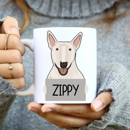 A person holding a white coffee mug with a black and grey Bull Terrier dog illustration on it, with the name 'Zippy' written on the mug.