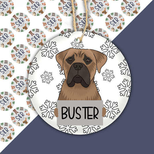 A ceramic Christmas ornament featuring a drawing of a Bullmastiff dog with snowflakes around it.