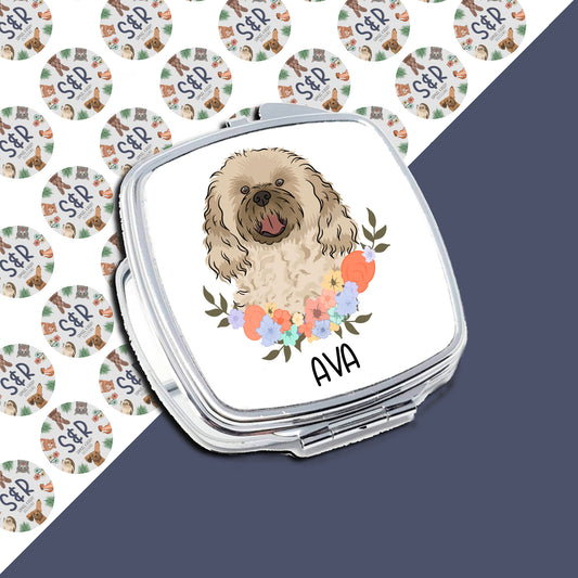 A personalised compact mirror with a cavapoo dog illustration and floral design, with the name 'Ava' on the image.