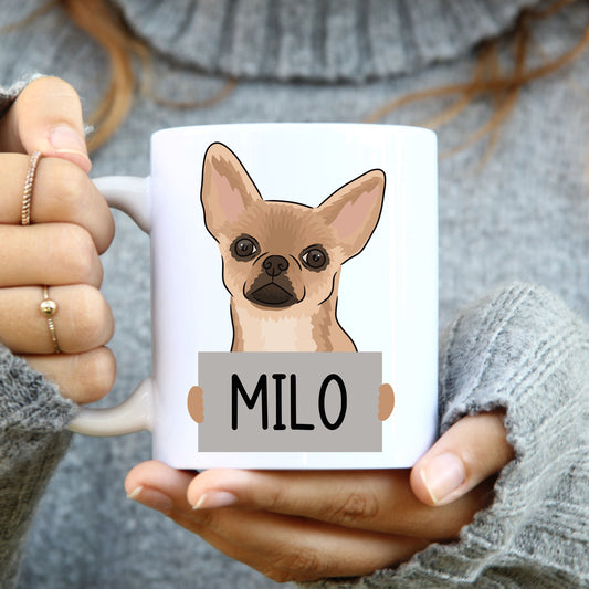 A person holding a white coffee mug with a colourful illustration of a Chihuahua dog on it.