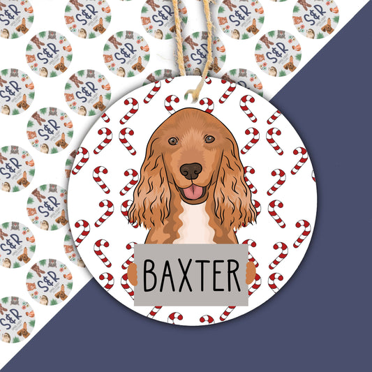 A ceramic Christmas ornament featuring an illustration of a Cocker Spaniel dog with a red and white color scheme and the name 'Baxter' on the lower part.