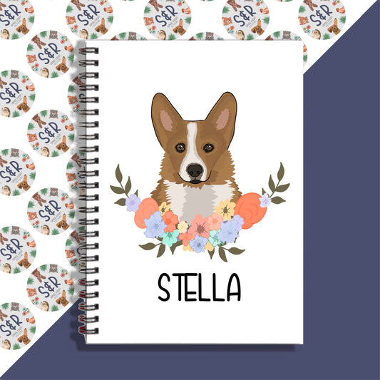 A personalised notebook with a graphic of a corgi dog on the front cover, surrounded by a floral pattern, with the name 'Stella' written on the notebook.