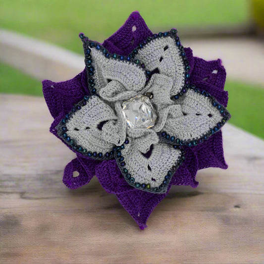 Crocheted lace flower brooch with purple and grey colors on a white background