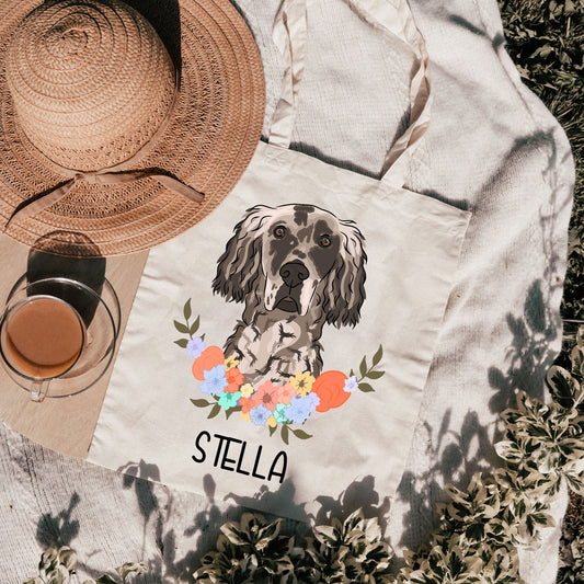 A white tote bag with a personalised print of an English Setter dog surrounded by a floral wreath, with the name 'Stella' printed on the bag.