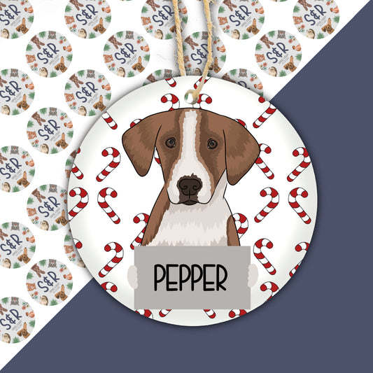 A ceramic Christmas ornament featuring an illustration of a foxhound dog with the name 'PEPPER' written on it, surrounded by Christmas-themed decorations like candy canes.