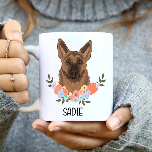 A white coffee mug with a printed illustration of a German Shepherd dog accompanied by a floral wreath, with the name 'Sadie' below the image.