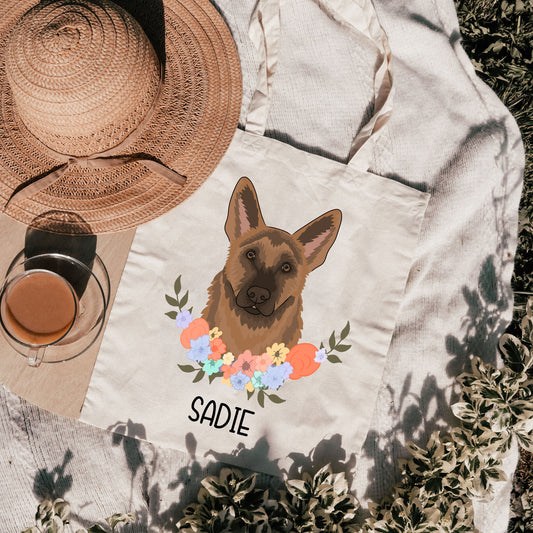 A white tote bag with a printed image of a German Shepherd dog surrounded by a floral wreath, with the name 'Sadie' printed on the front.