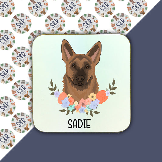 A square coaster with a illustration of a German Shepherd dog surrounded by a floral wreath, with the name 'Sadie' at the bottom.