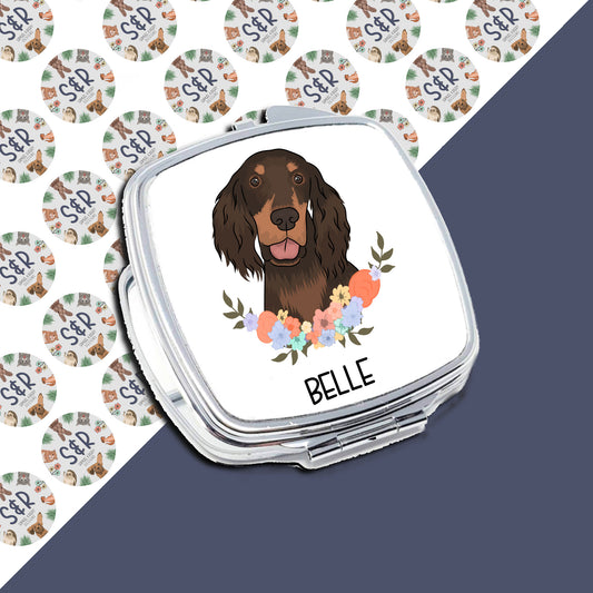 A personalised compact mirror with an illustration of a dog, resembling a Gordon Setter, surrounded by a floral pattern on the front.