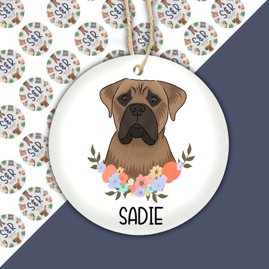 A round ceramic Christmas decoration featuring a hand-painted illustration of a Great Dane dog with a floral wreath in the background, with the name 'Sadie' underneath the image.