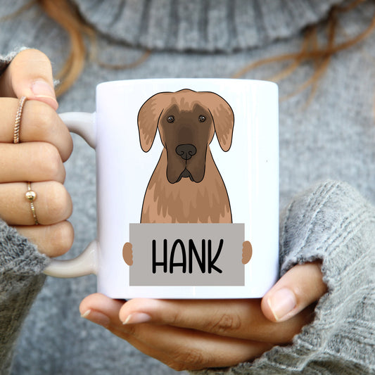 A person holding a white coffee mug with a colourful illustration of a Great Dane dog on it.
