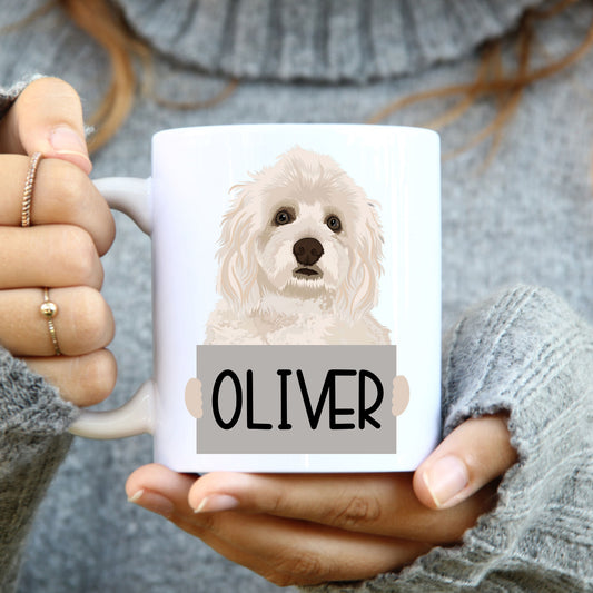 A person holding a white coffee mug with a printed image of a Havanese dog on the side, with the name 'Oliver' below the image.