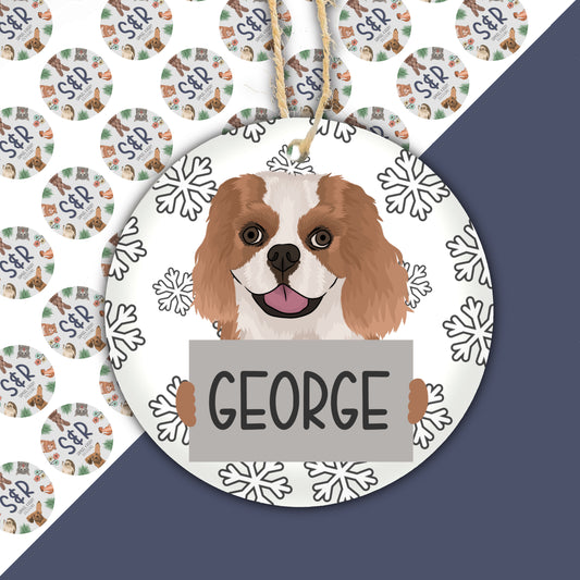 A ceramic Christmas decoration featuring a drawing of a King Charles Spaniel dog with the name 'George' written on the ornament.