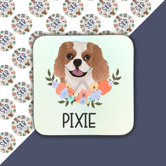 A square coaster with a printed image of a King Charles Spaniel dog surrounded by a floral pattern.