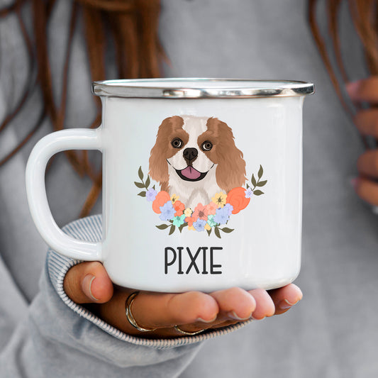 A white ceramic enamel mug with a printed image of a King Charles Spaniel dog surrounded by a floral pattern, with the name 'PIXIE' inscribed at the bottom.