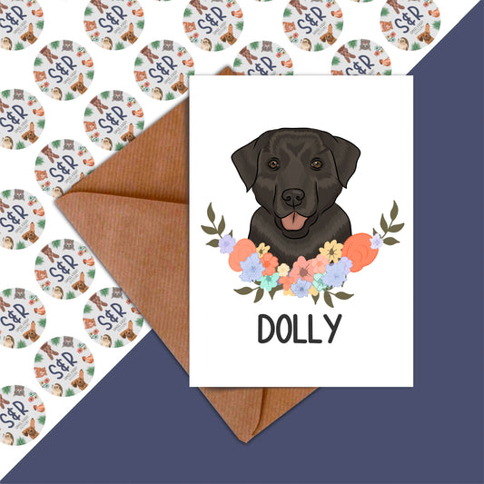 A greeting card featuring an illustration of a black Labrador dog with a floral wreath and the name 'Dolly' on the front.