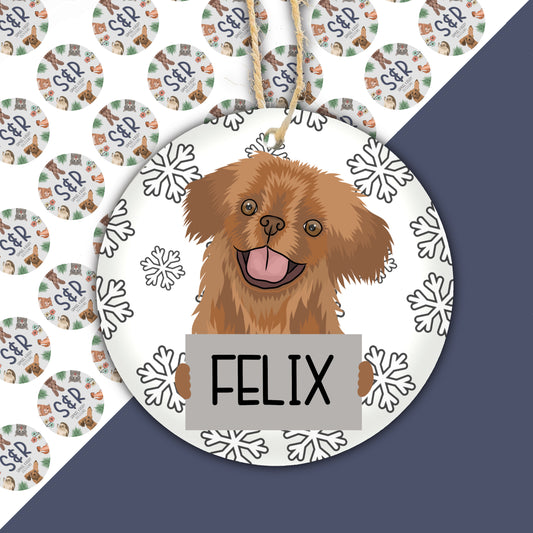 A ceramic Christmas decoration featuring a cartoon illustration of a Pekingese dog with the name 'Felix' on the ornament, surrounded by snowflake designs.