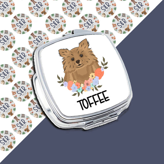 A personalised compact mirror with a Pomeranian dog illustration and the name 'Tofee' on the front, surrounded by a floral pattern.