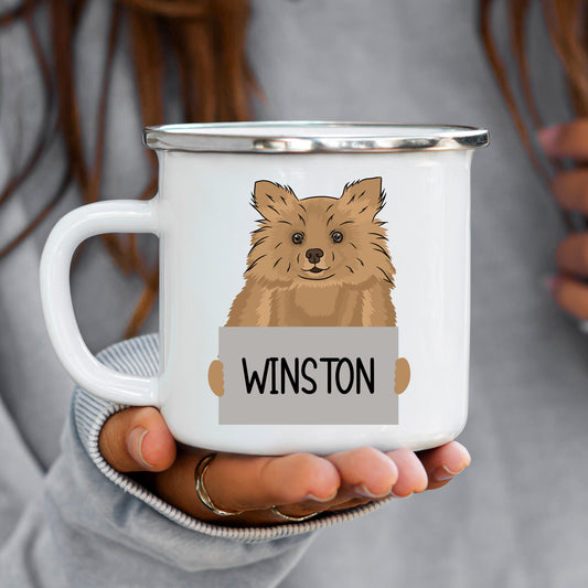 A white enamel mug with a illustration of a Pomeranian dog breed, held in a person's hand.