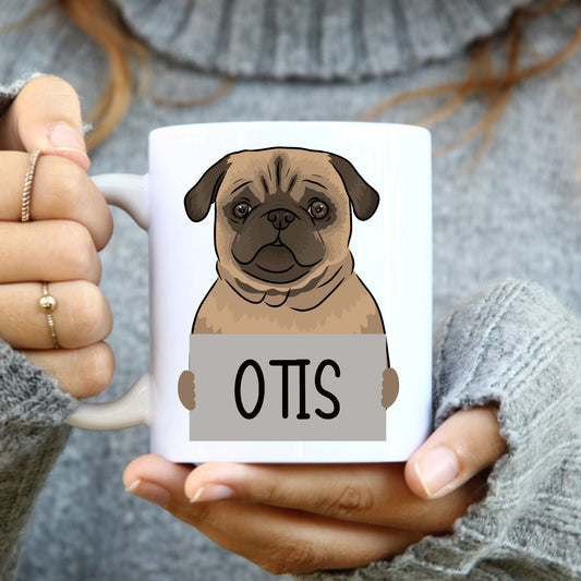 A person holding a white ceramic mug with a printed pug dog design and the name 'Otis' on it.