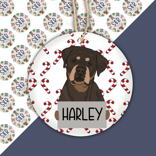 A ceramic Christmas ornament featuring an illustration of a Rottweiler dog with a Santa hat, part of a Christmas decoration collection.