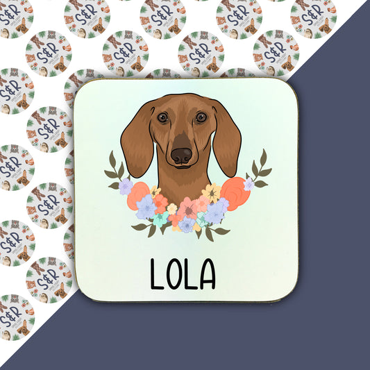 A square coaster with a cartoon illustration of a sausage dog in the center surrounded by a floral pattern.