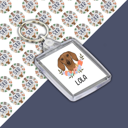 A personalised double-sided acrylic keyring featuring an illustration of a sausage dog breed, with the name 'LOLA' printed on it.