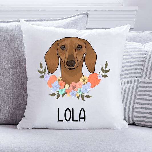 A square-shaped cushion with a white background featuring an illustration of a sausage dog (dachshund) in the centre surrounded by a floral pattern. The cushion has the text 'LOLA' near the bottom.