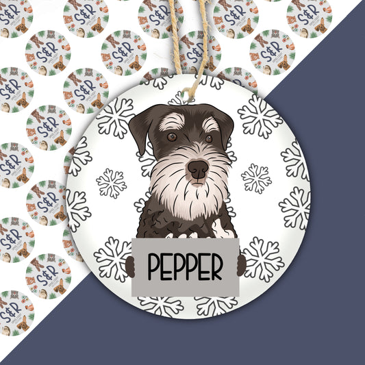 A ceramic Christmas decoration featuring a cartoon illustration of a Schnauzer dog with snowflakes and the name 'PEPPER'.