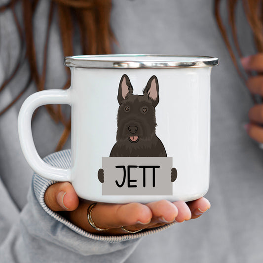 A white enamel mug with a graphic of a Scottish Terrier dog at the top, held in a person's hand.