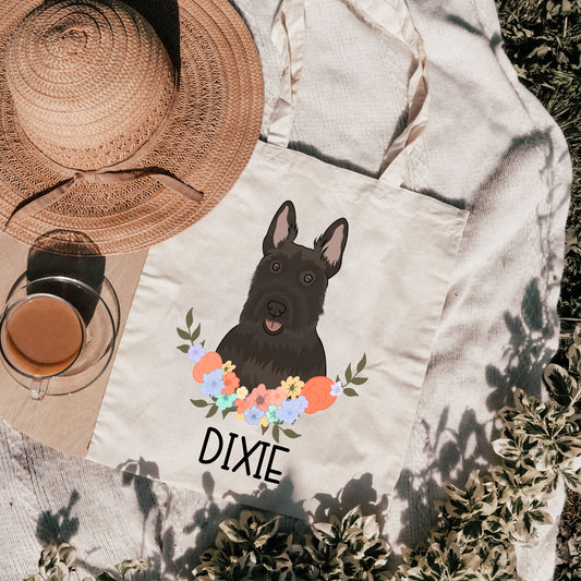 A canvas tote bag with a printed image of a Scottish Terrier dog surrounded by a floral wreath, with the text 'DIXIE