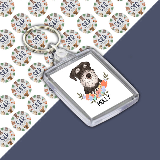 A personalised double-sided Schnauzer dog keyring in a clear acrylic casing, featuring an illustration of a Schnauzer dog on a branded design.