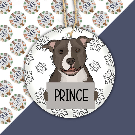 A round ceramic pet bauble featuring an illustration of a dog with the name 'Prince' written on it, set against a snowflake pattern background.