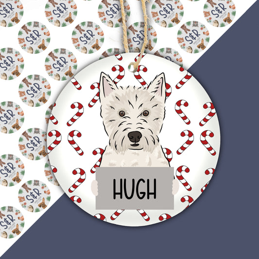 A ceramic Christmas ornament featuring a Westie dog design with the name 'Hugh' written on it, surrounded by Christmas-themed patterns.