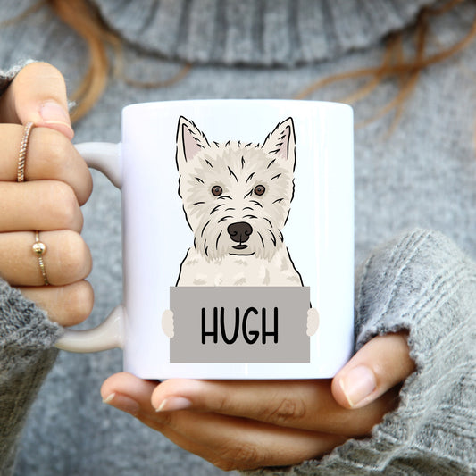 A person holding a white coffee mug with a graphic of a West Highland Terrier dog on it, with the name 'Hugh' printed on the mug.
