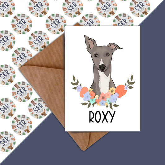 A Whippet dog illustrated on a birthday card with a floral wreath background, accompanied by a brown envelope.
