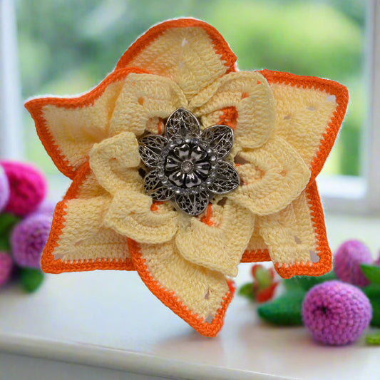 Star-shaped brooch with orange and beige flower design and silver center on a blurred background